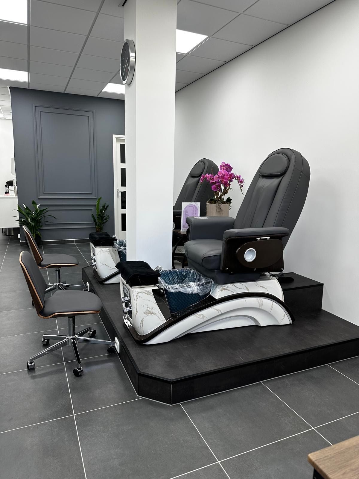 Twee pedicurestoelen op een podium in de salon van Livi Nails, met een roze orchidee