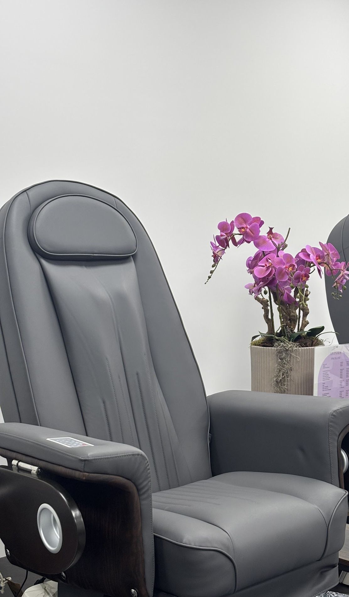 Een grijze pedicurestoel met een roze orchidee en de prijslijst van Livi Nails ernaast