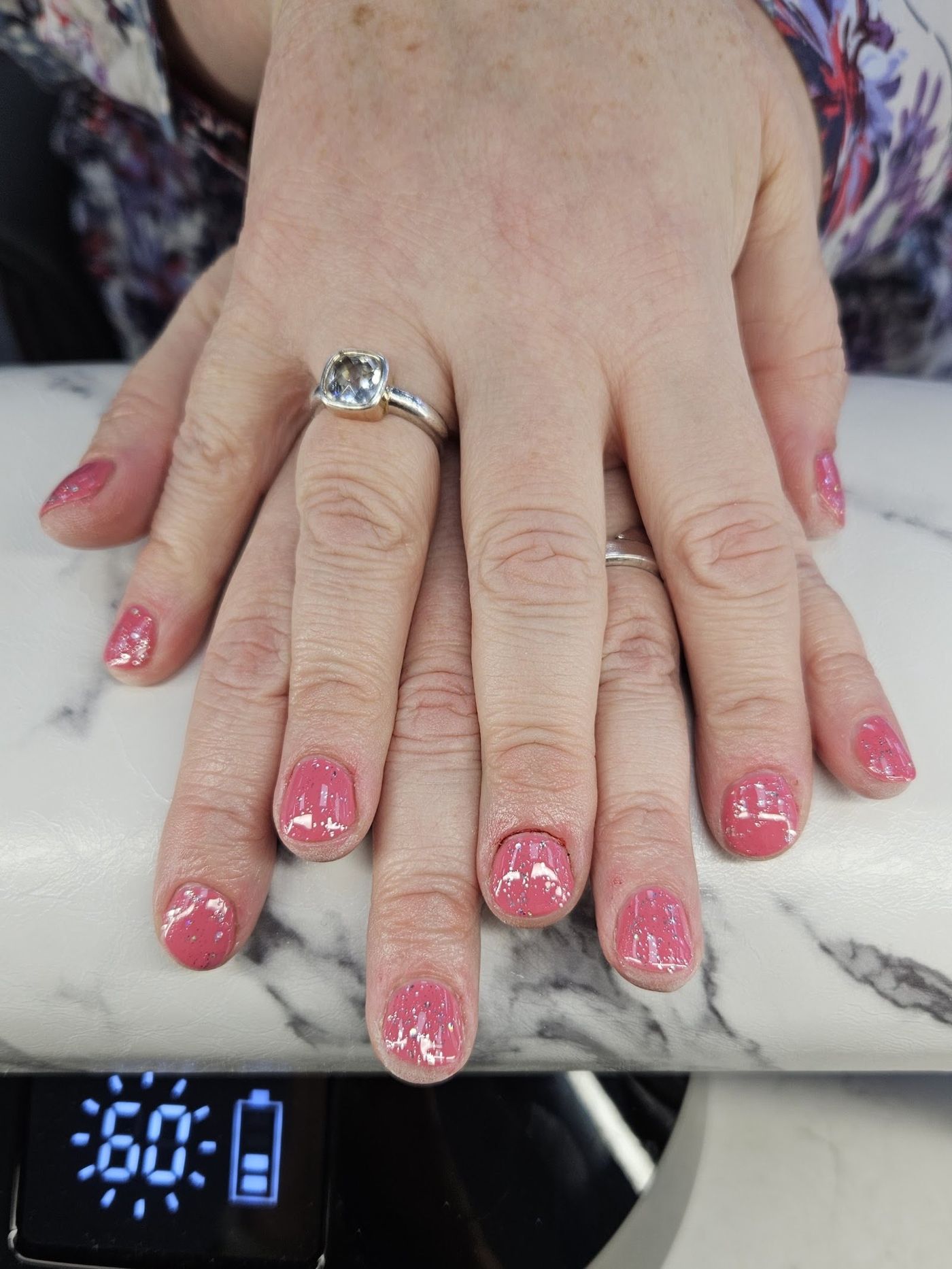 Roze gellak met glitter op korte nagels, op de marmeren armsteun